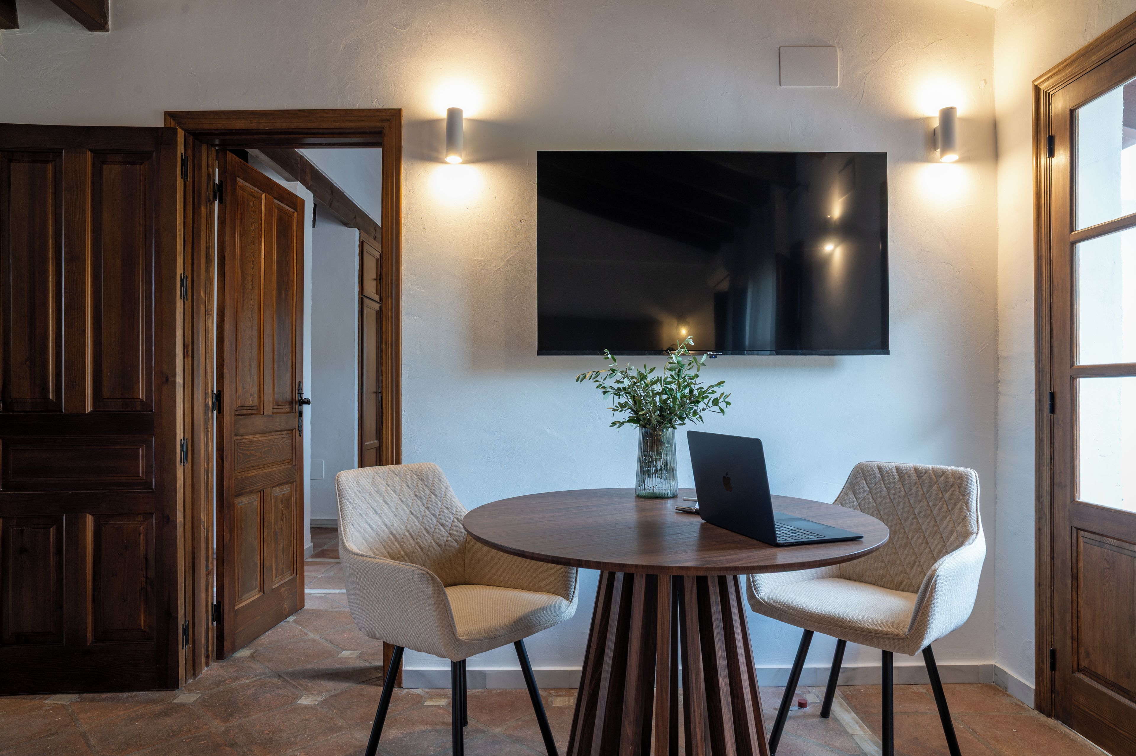 A conference room with a round table, two chairs, a laptop, and a potted plant.