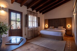 A bedroom with a bed, bedside lamps, a window with curtains, a door, and a small table with a book. - Malaga Sierra de las Nieves by Real Spain Hotels (Casarabonela)