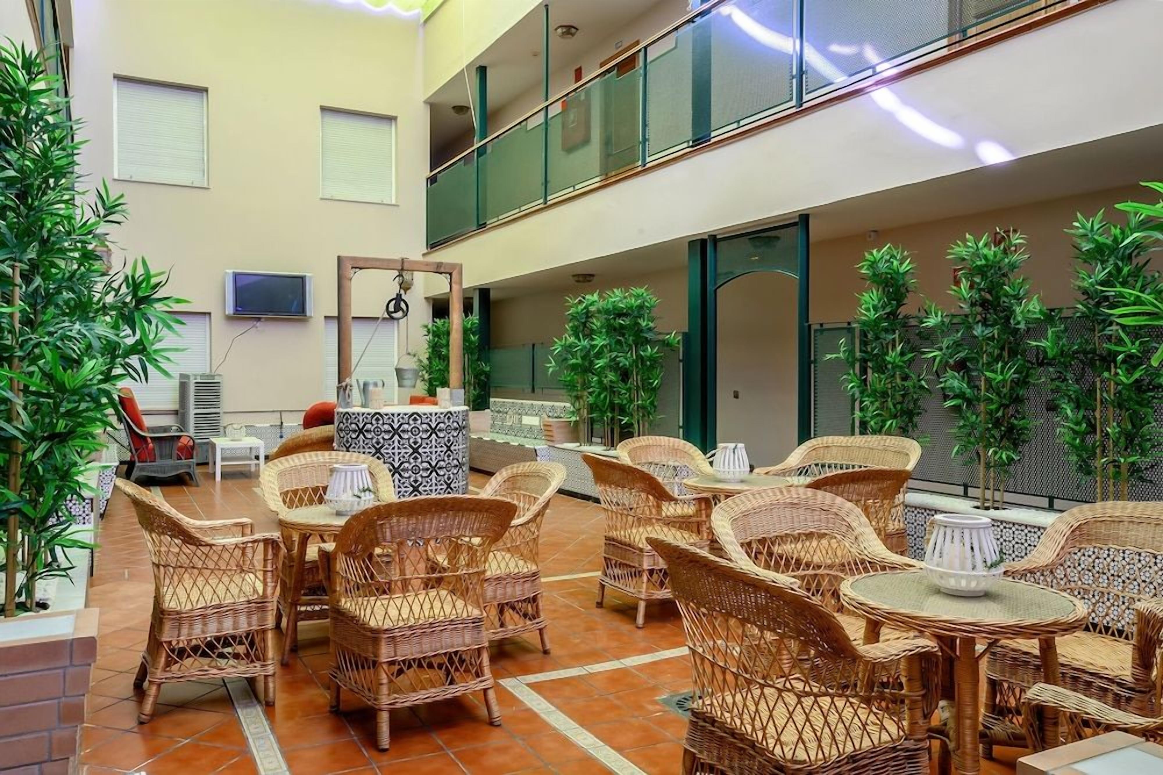 Un amplio patio interior con mobiliario de mimbre, plantas en macetas y un televisor montado en la pared.