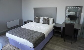 A modern bedroom with a bed, bedside tables, a dresser, and a mirror.