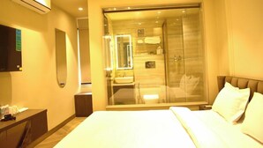 A hotel room with a bed, a bedside table, a mirror, a wardrobe, and a shower area visible through a glass door. - Hotel Cullinan By Qotel (New Delhi)