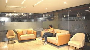 A modern waiting area with a sofa, chairs, and a glass partition. - Hotel Cullinan By Qotel (New Delhi)