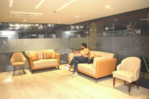 A modern waiting area with a sofa, chairs, and a glass partition. - Hotel Cullinan By Qotel (New Delhi)