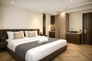 Una habitación de hotel moderna con una cama grande, una mesita de noche, un armario y una pequeña zona de kitchenette.