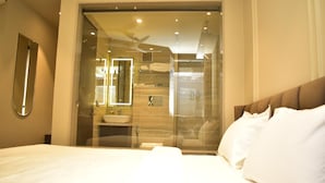A hotel room with a bed, a bathroom visible through a glass door, and a ceiling fan. - Hotel Cullinan By Qotel (New Delhi)