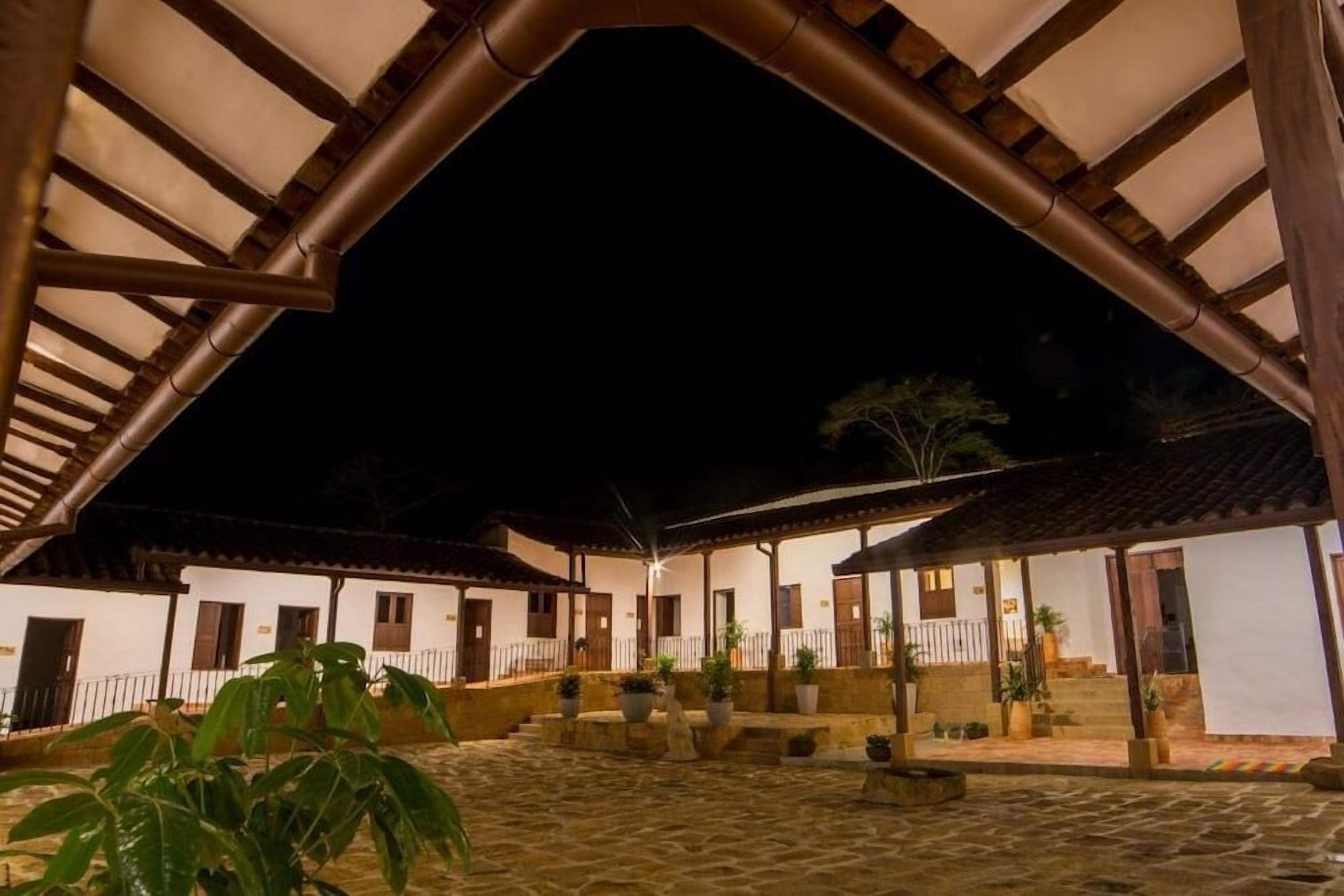 A courtyard with a covered walkway, potted plants, and a building with multiple doors and windows.
