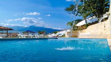 A swimming pool with clear blue water, a few lounge chairs, and a mountainous backdrop.