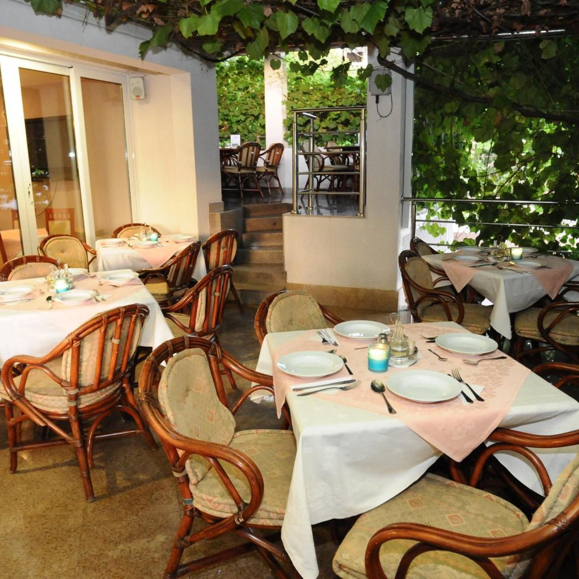 An outdoor dining area with tables and chairs, a staircase, and a view of greenery.
