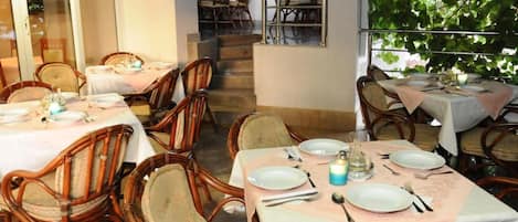 An outdoor dining area with tables and chairs, a staircase, and a view of greenery.