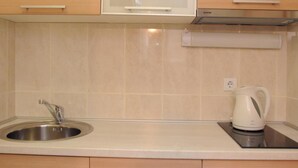 Una cocina con un lavamanos de acero inoxidable, un hervidor blanco y armarios de madera.