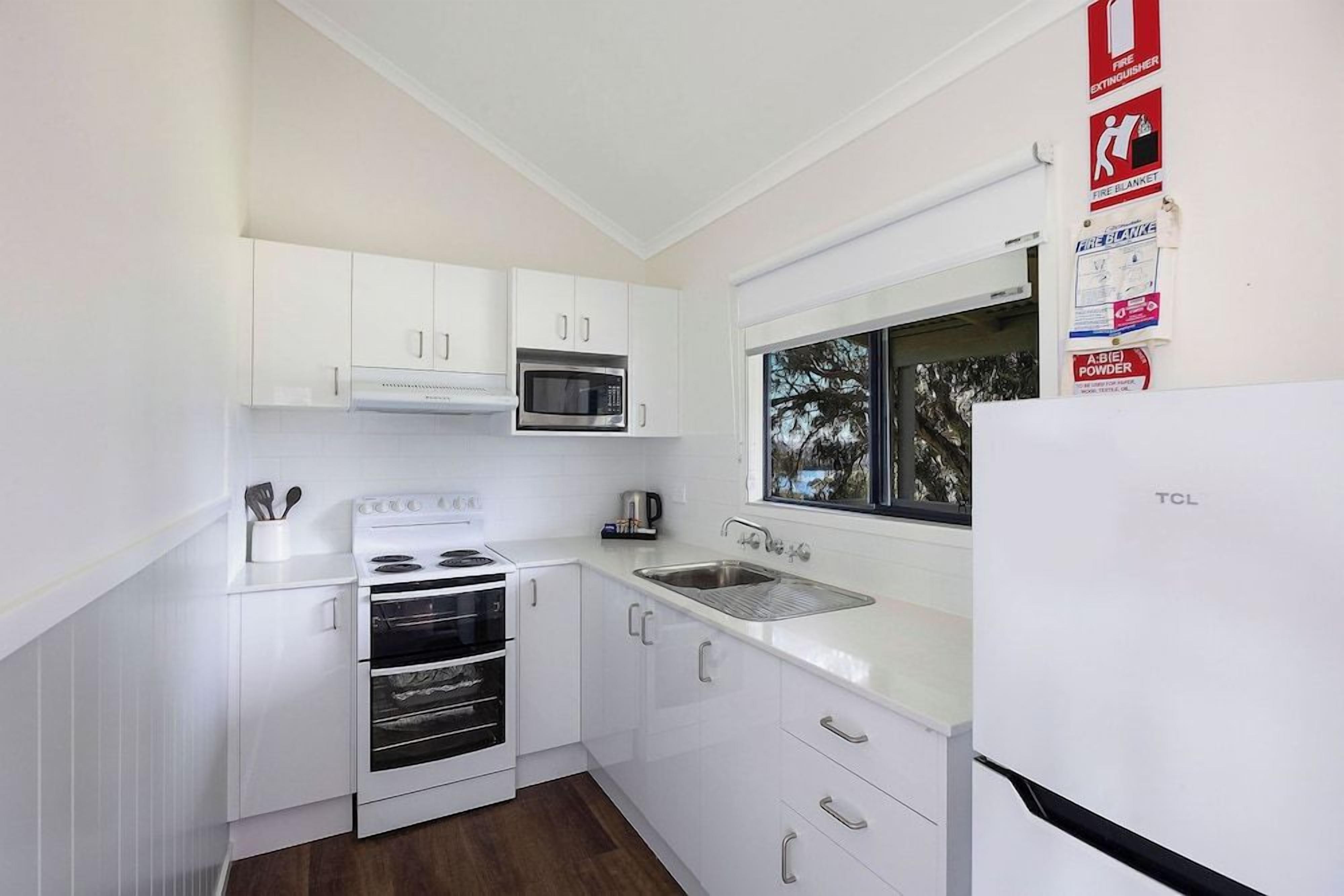 A modern kitchen with white cabinetry, a microwave, a stove, and a sink. There are fire safety signs on the wall.