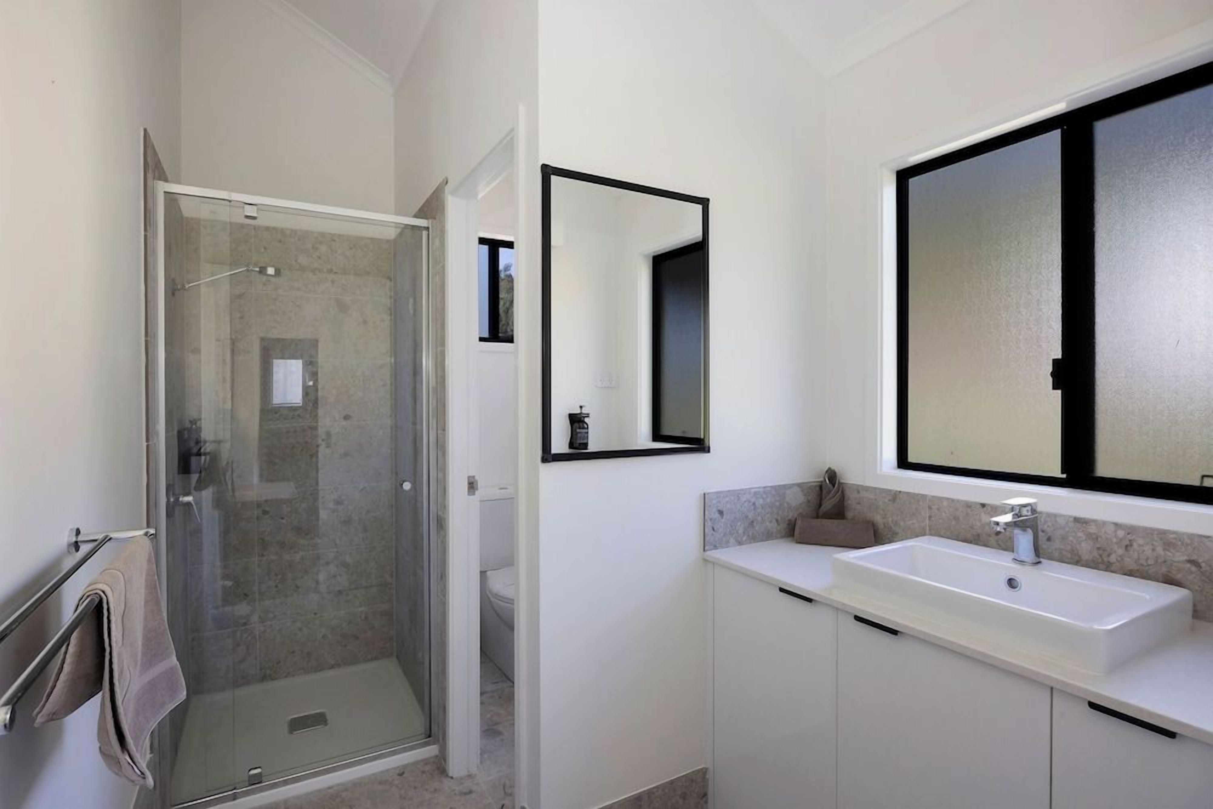 A modern bathroom with a glass shower enclosure, a large mirror, and a white sink.