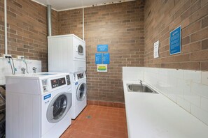 Una sala de bugaderia amb dues rentadores, un safareig i diversos senyals amb instruccions d'ús.