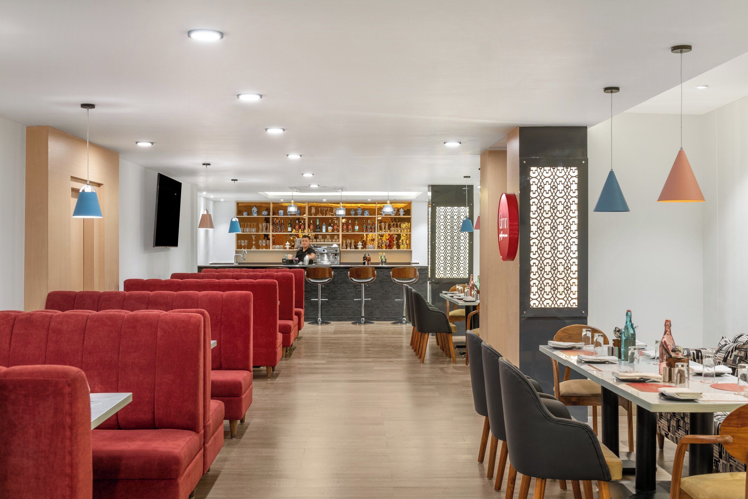 Un restaurante con asientos tapizados en rojo, una zona de bar con estantes llenos de botellas, e iluminación colgante.