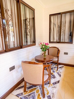 A corner room with a dining table, two chairs, a vase with flowers, and decorative iron bars on the windows. - Light Villas (Nairobi)