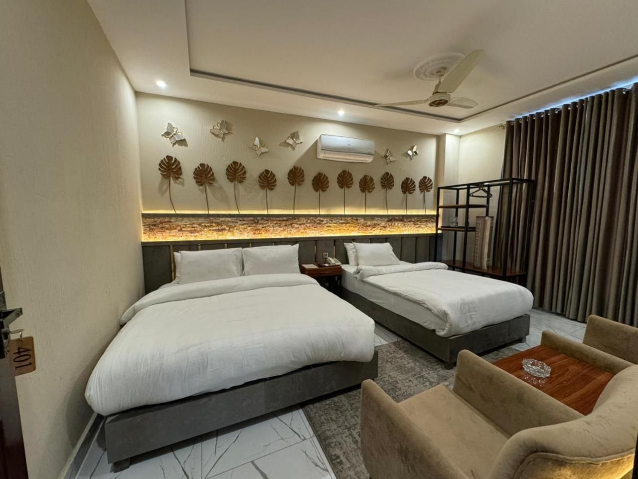A hotel room with two beds, a seating area, and a decorative wall with leaf patterns.