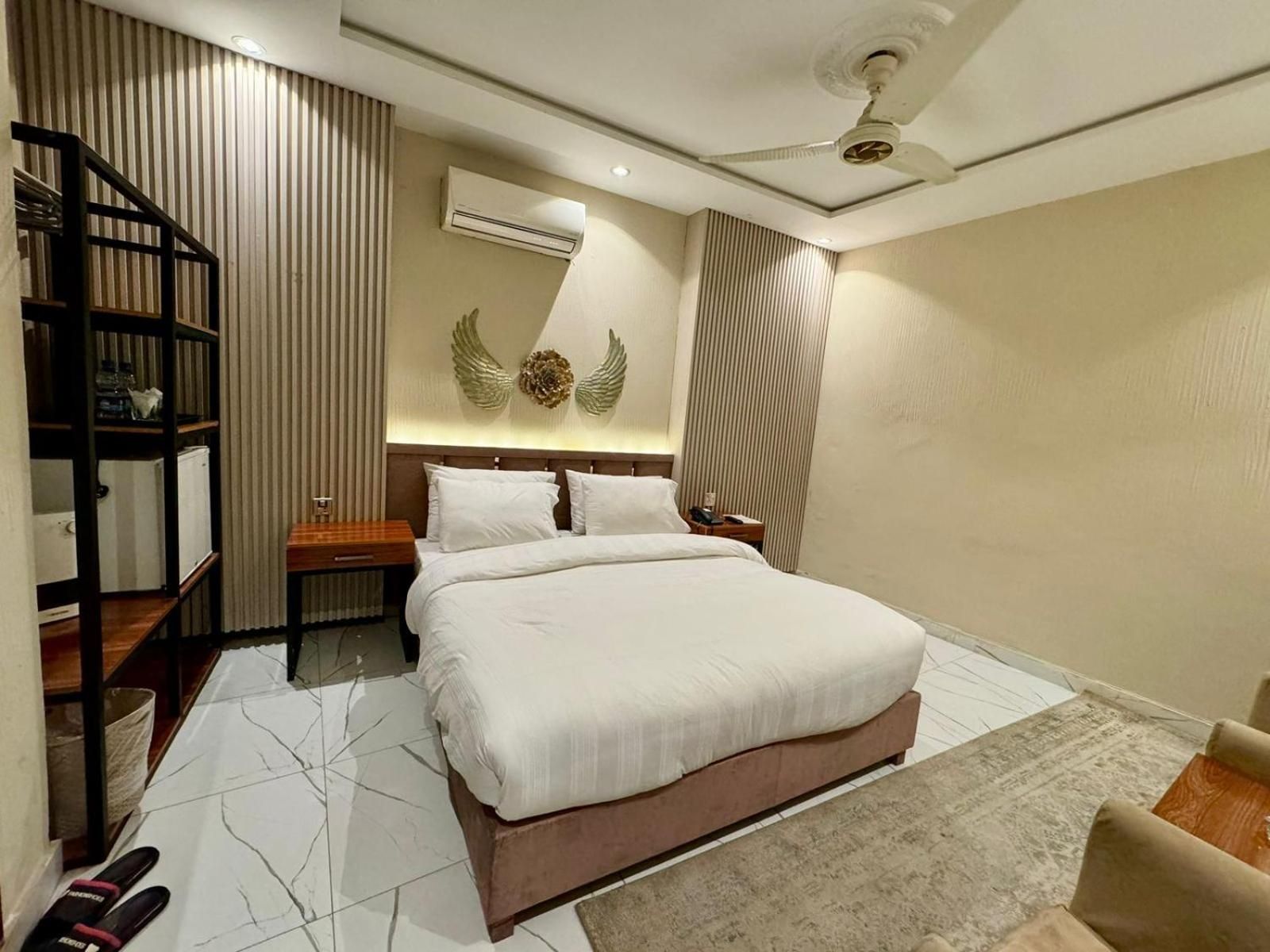 A hotel room with a bed, a nightstand, a wall-mounted air conditioner, a ceiling fan, and a built-in bookshelf.