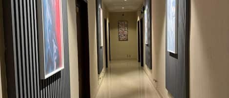 A hallway with a tiled floor, flanked by walls with vertical paneling, and doors leading to rooms.