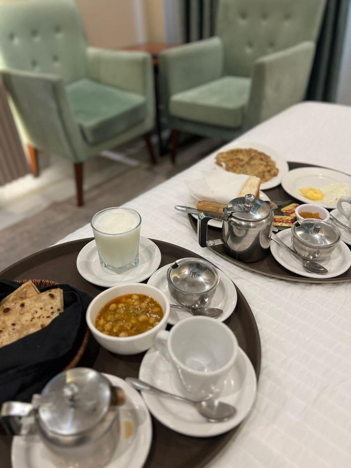 A breakfast tray with various dishes including flatbread, a bowl of chickpeas, a glass of milk, and a teapot.
