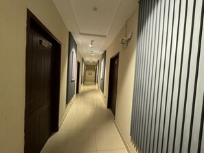 Pasillo de hotel con puertas a ambos lados, piso de baldosas e iluminación empotrada en el techo.