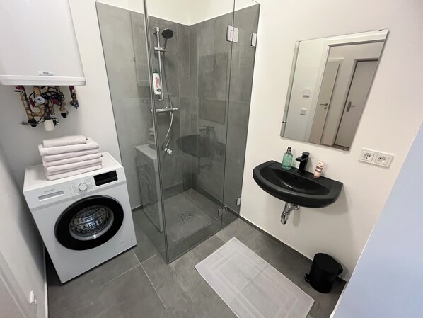 Un baño moderno con ducha de vidrio, lavadora, lavamanos y espejo.