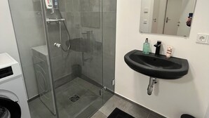 Ein modernes Badezimmer mit einer Glaskabine zur Dusche, einem schwarzen Waschbecken und einem Spiegel darüber.