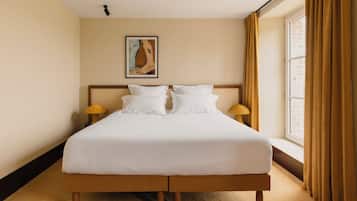 Una habitación de hotel con una cama grande, dos lámparas de noche, un cuadro en la pared y una ventana con cortinas.