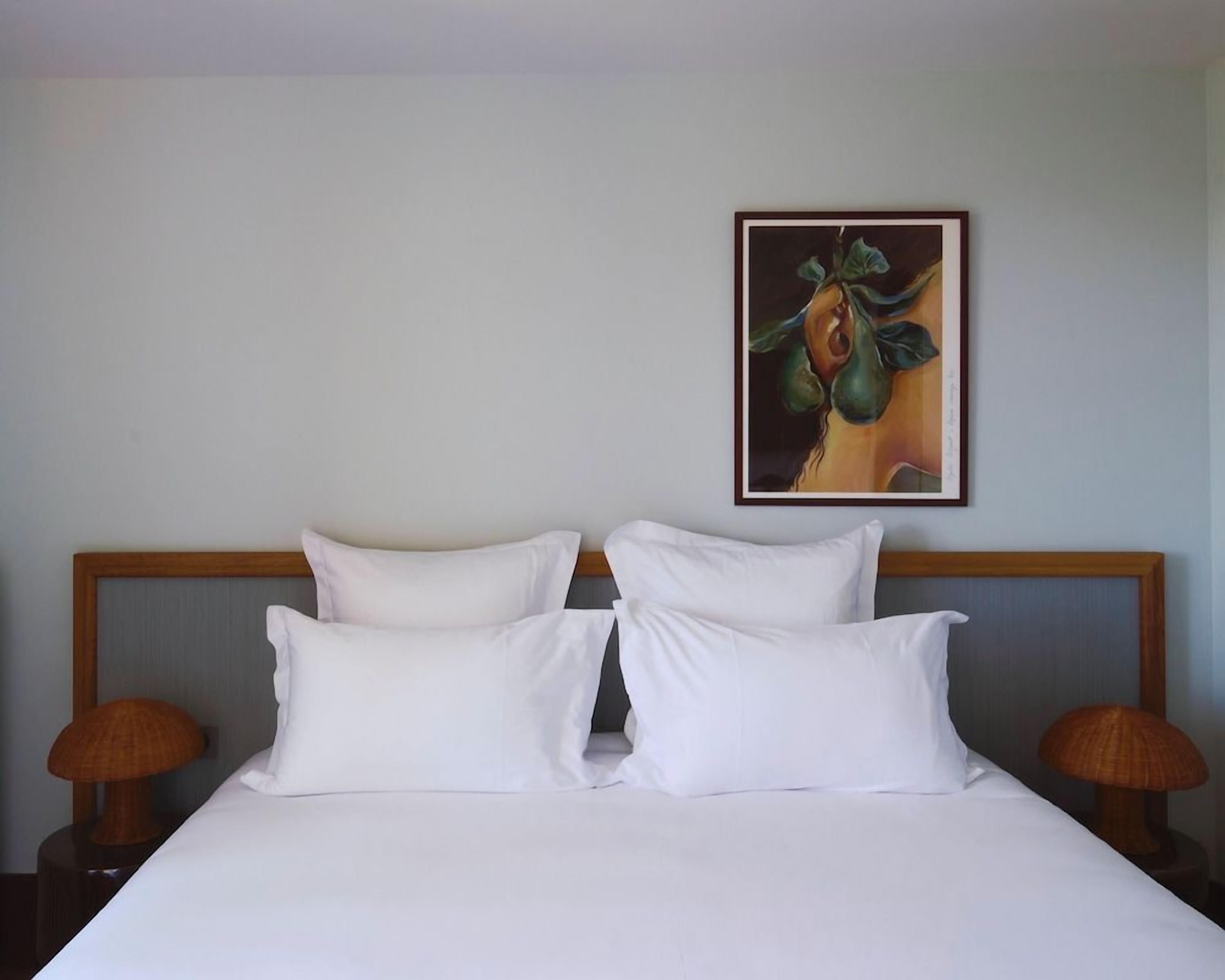 Una camera d'albergo con un letto, due cuscini, una testiera, un quadro appeso al muro e due lampade su comodini.