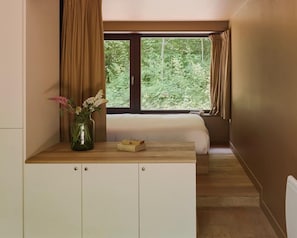 Un dormitorio con cama, un escritorio de madera, un florero con flores y una ventana con cortinas.