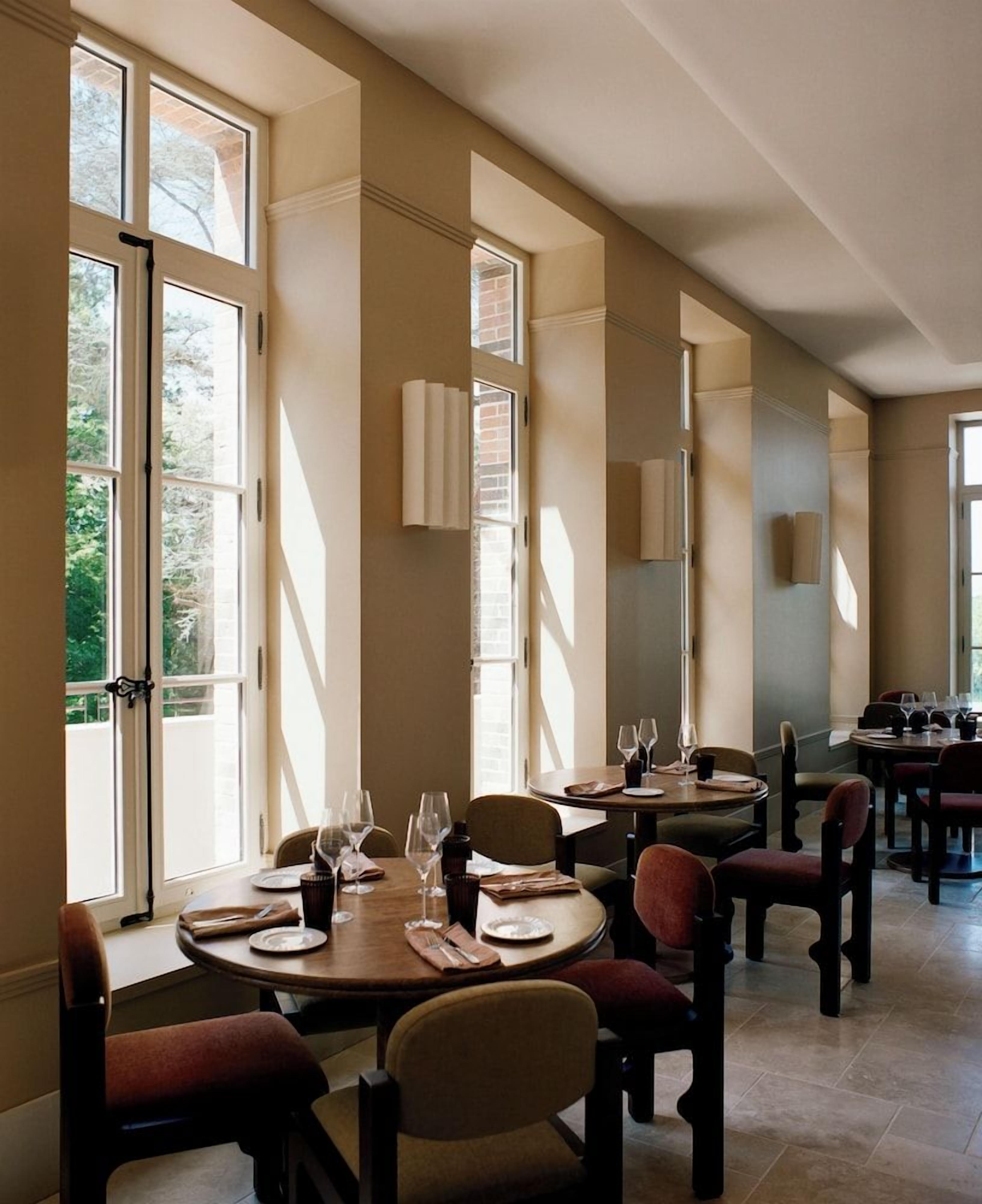 A dining area with multiple tables, chairs, and a view of the outdoors through large windows.