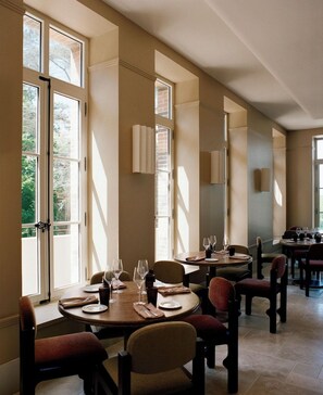 Un espace repas comprenant plusieurs tables, des chaises et offrant une vue sur l’extérieur grâce à de grandes fenêtres.