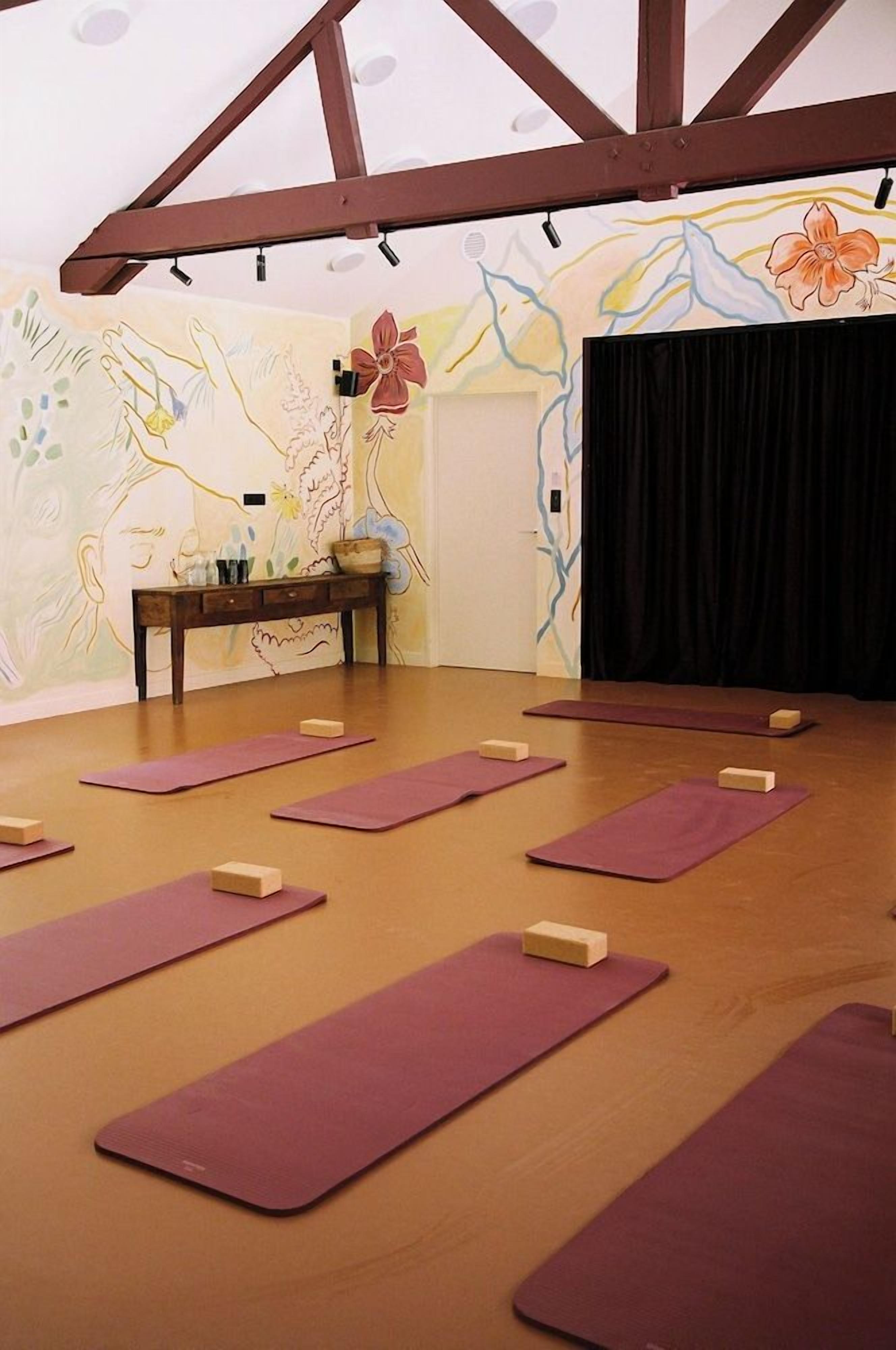 Un estudio de yoga con vigas de madera, un mural y esterillas moradas.