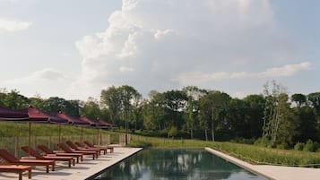 Et poolområde med liggestole og parasoller, omgivet af træer og en klar himmel.