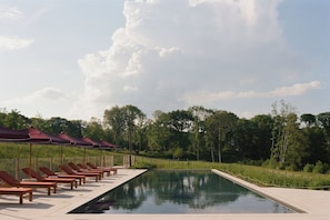 Un espace aménagé au bord de la piscine, avec des chaises longues et des parasols, entouré d’arbres et surplombé par un ciel dégagé.