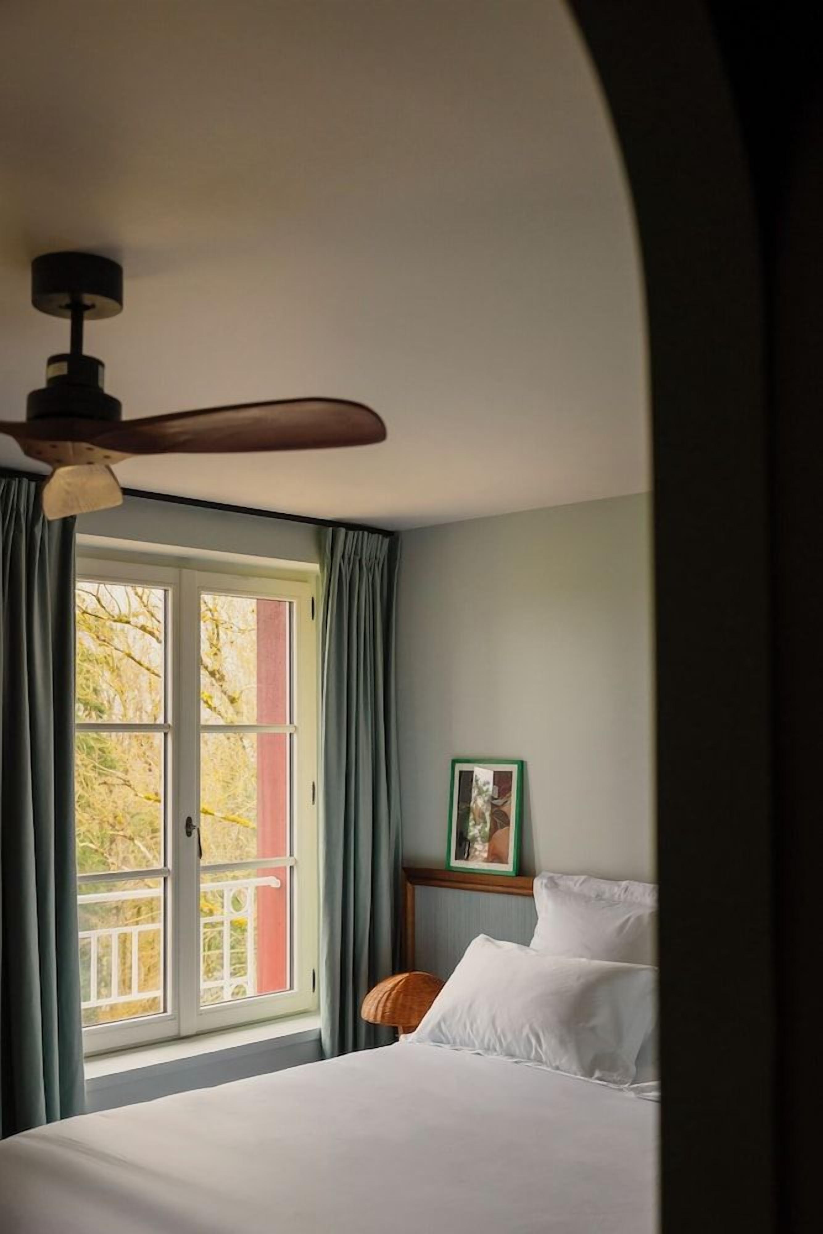 A bedroom with a bed, a ceiling fan, a window with curtains, and a framed picture on the wall.