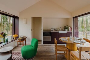 Una cocina moderna con armarios oscuros, un comedor con una mesa redonda y una silla verde.
