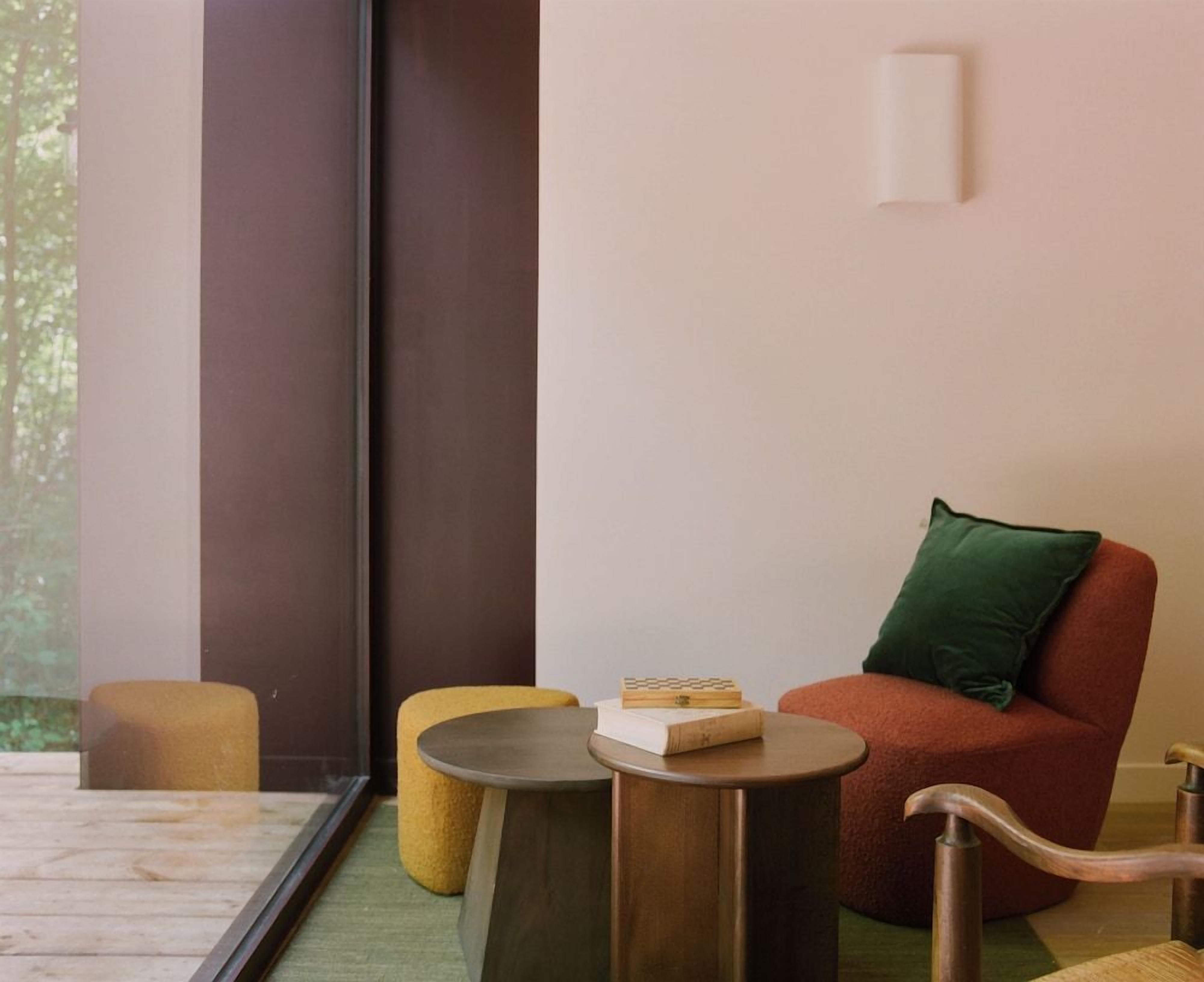 A modern room with a large window, a red chair, a yellow stool, and a small round table with a book on it.