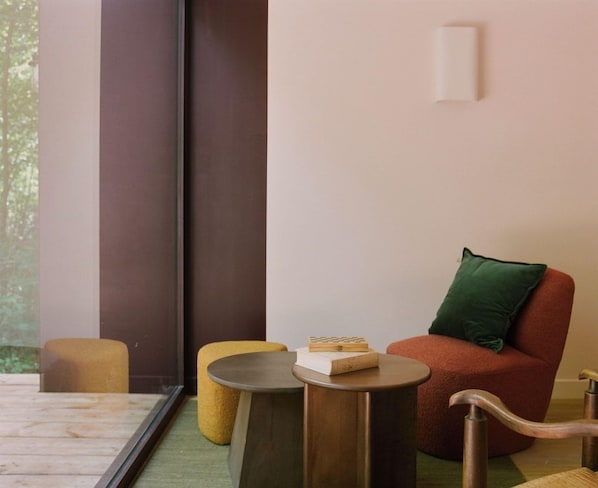 A modern room with a large window, a red chair, a yellow stool, and a small round table with a book on it.
