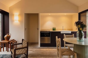 A modern kitchen with dark cabinetry, a built-in oven, and a dining area with a round table and woven chairs.