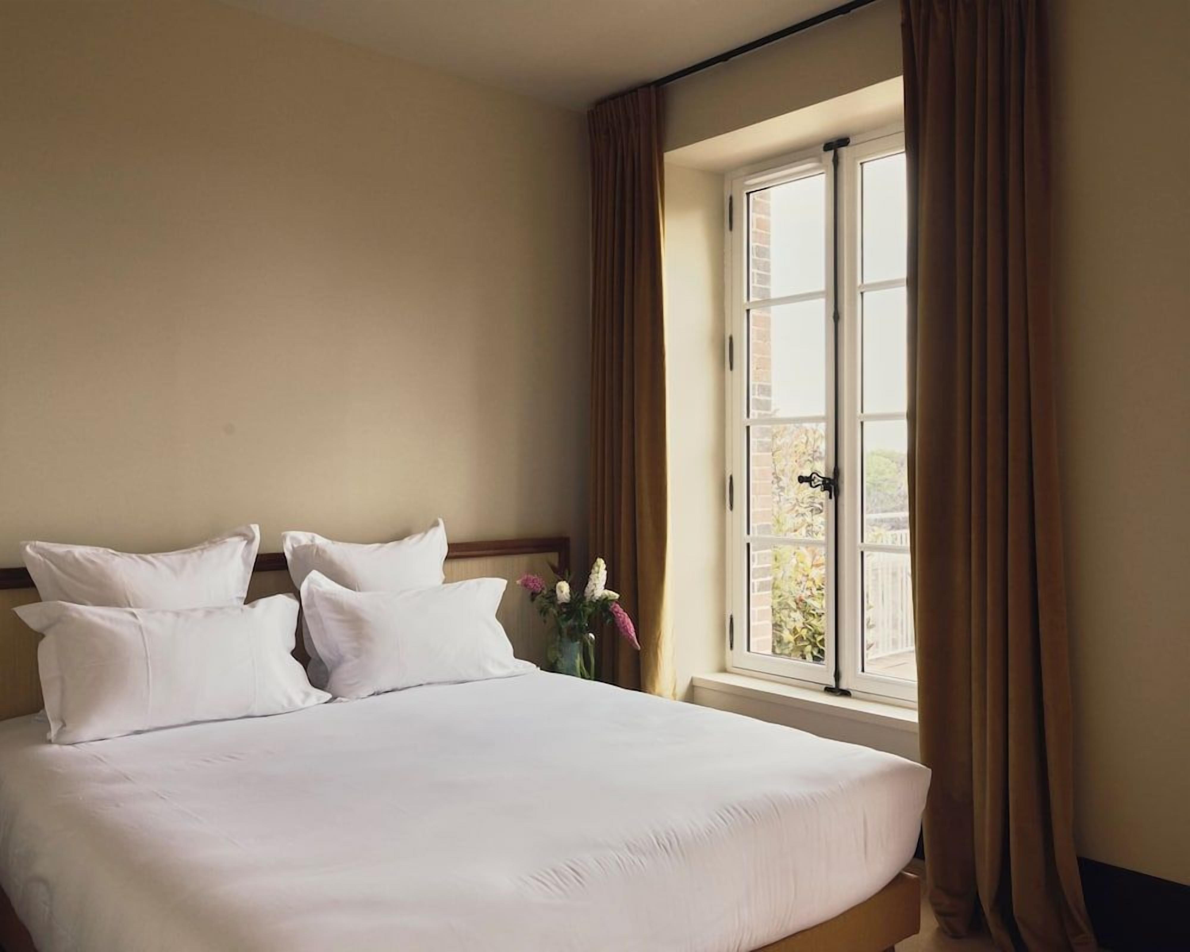 A hotel room with a large bed, a window with curtains, and a view of the outside.