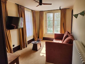 A living room with a sofa, a coffee table, a flat-screen TV, and a window with curtains.