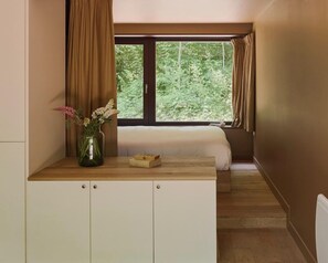 Une chambre à coucher avec un lit, un bureau en bois, un vase de fleurs et une fenêtre avec des rideaux.