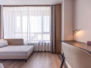 Une chambre d’hôtel avec un lit, un bureau, une lampe et une vue à travers des rideaux transparents.