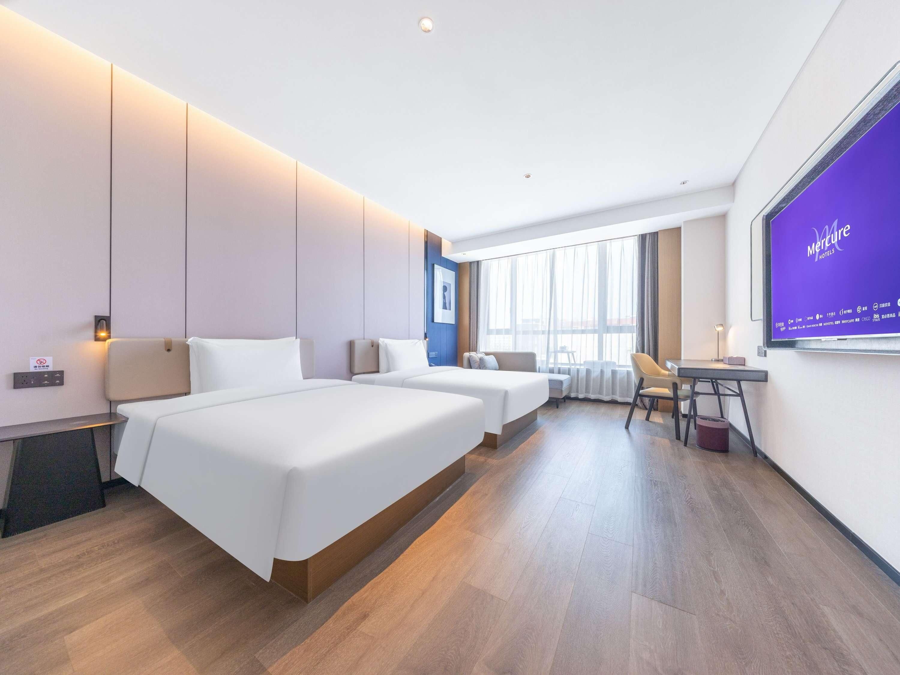 A hotel room with two beds, a desk, a chair, and a large window.