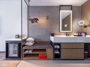 A modern bathroom with a large mirror, a towel rack, a sink with toiletries, and a built-in storage unit.