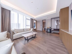 A modern hotel room with a sofa, a coffee table, and a kitchenette area. - Mercure Jinan Beiyuan Street (Jinan)