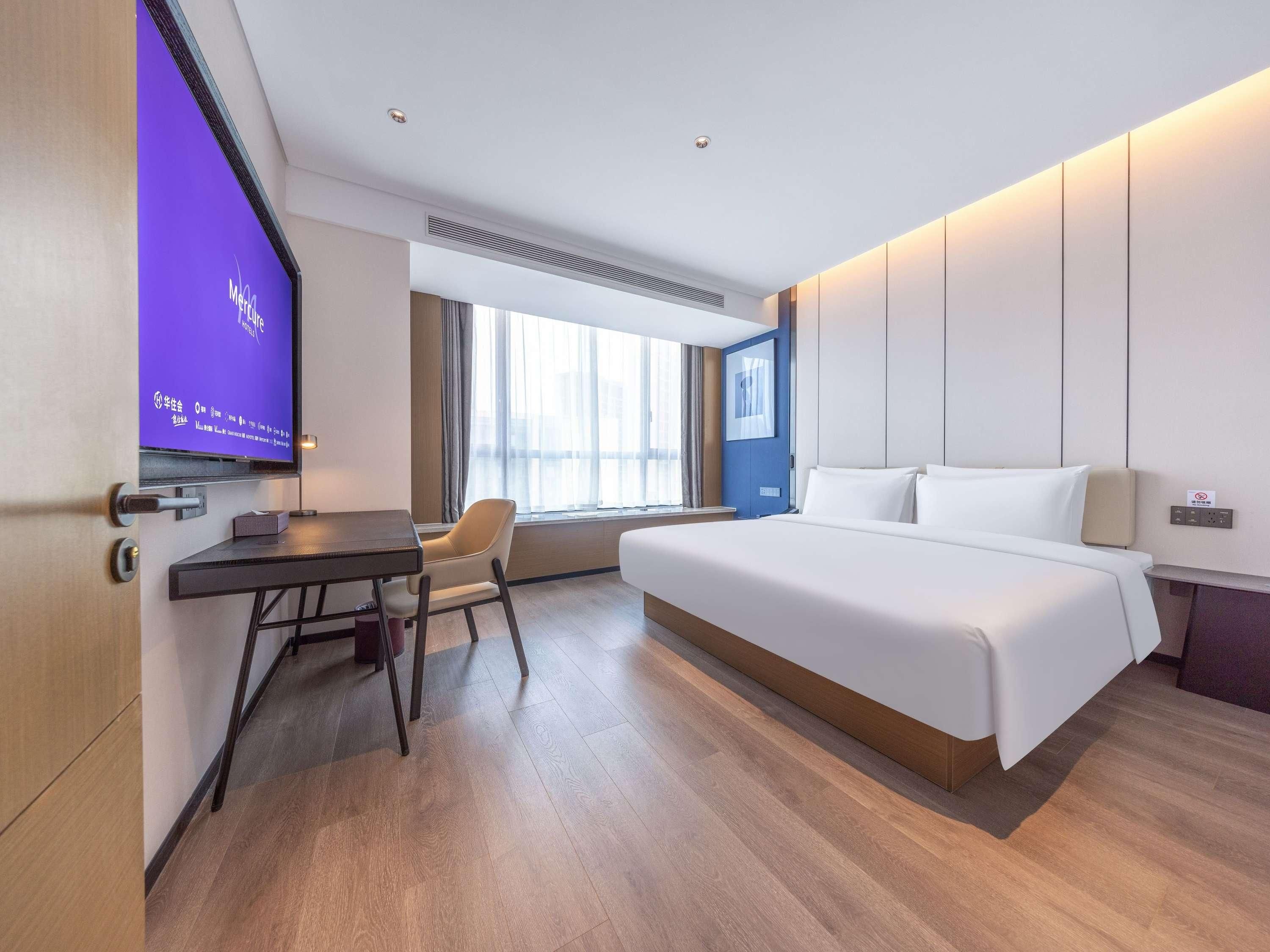Ein Hotelzimmer mit einem Bett, einem Schreibtisch, einem Stuhl, einem Fernseher und einem Fenster.