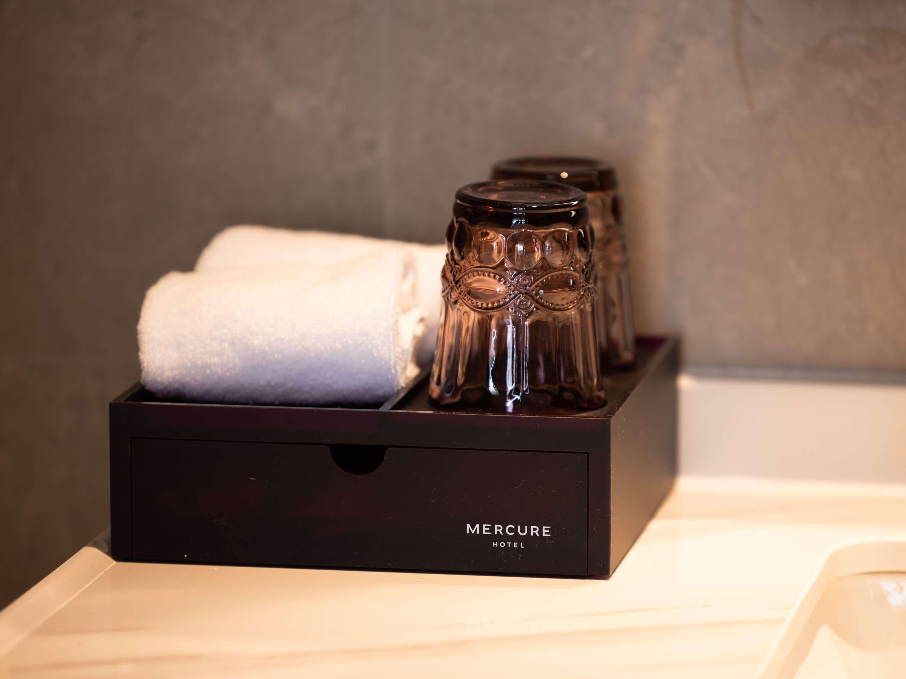 Une boîte noire portant l’étiquette « HÔTEL MERCURE », contenant une serviette blanche pliée et trois salières et poivrières.