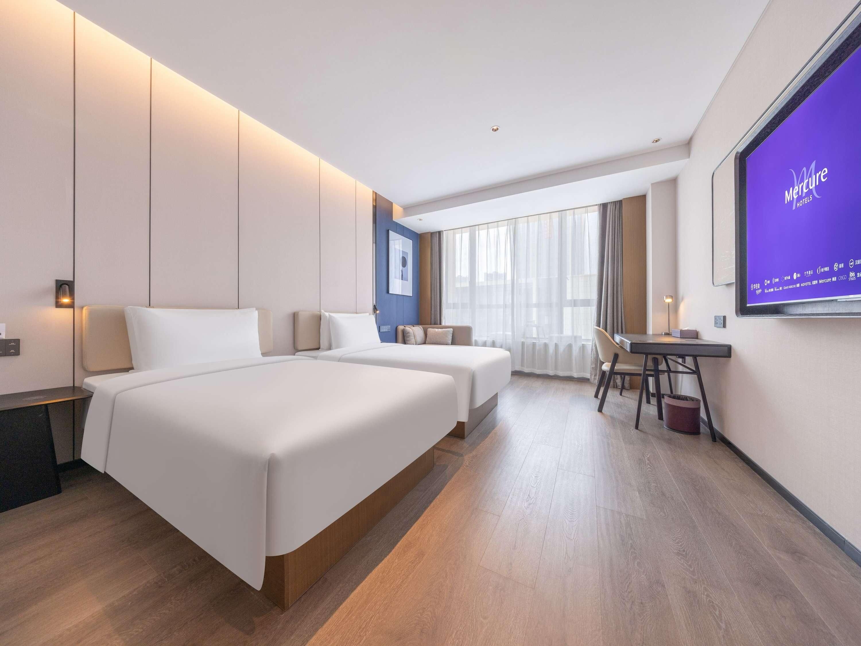 Een moderne hotelkamer met twee bedden, een bureau en een groot scherm waarop de naam van het hotel staat.