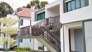 Um edifício residencial moderno com escada que leva a uma varanda, cercado por vegetação.
